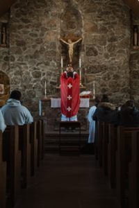 Un sacerdote se para frente a un altar dentro de una iglesia, elevando la copa eucarística. 