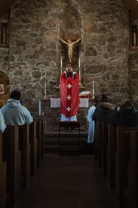 A priest stands in front of an altar inside a church, elevating the Eucharistic cup. 