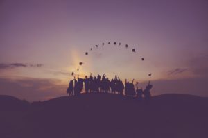 Silhouette of graduates tossing their caps in the air in an arc at sunset. 