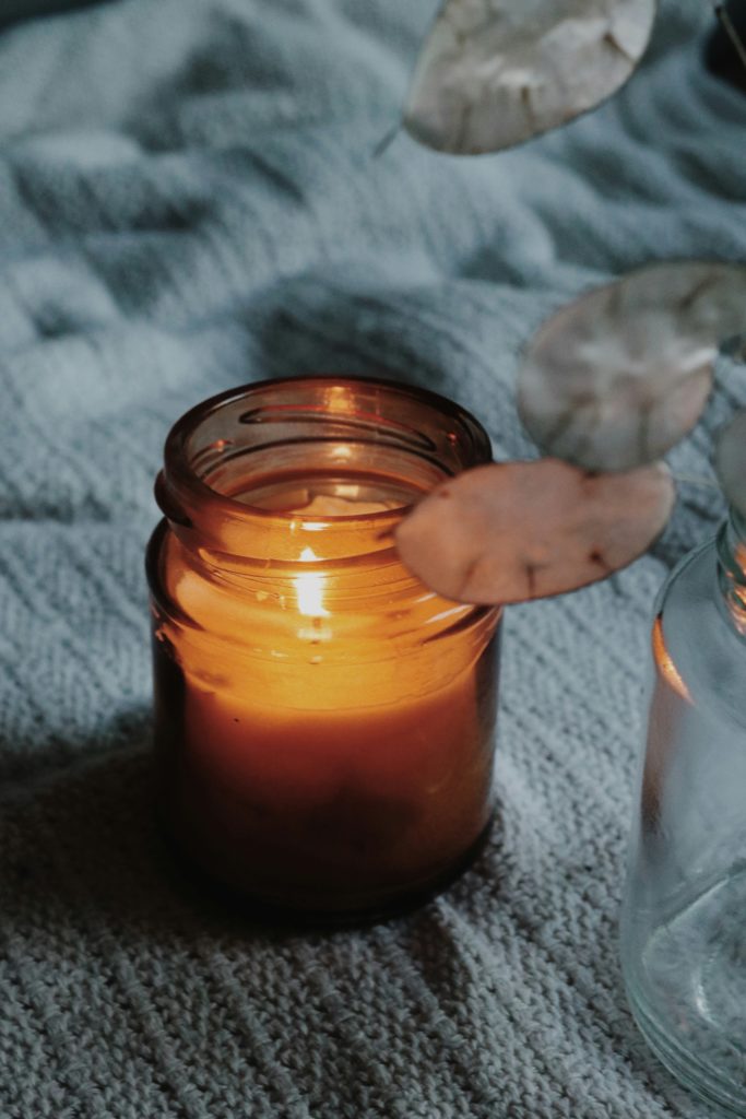 A photograph of a lit candle in a jar sitting on a gray blanket. 